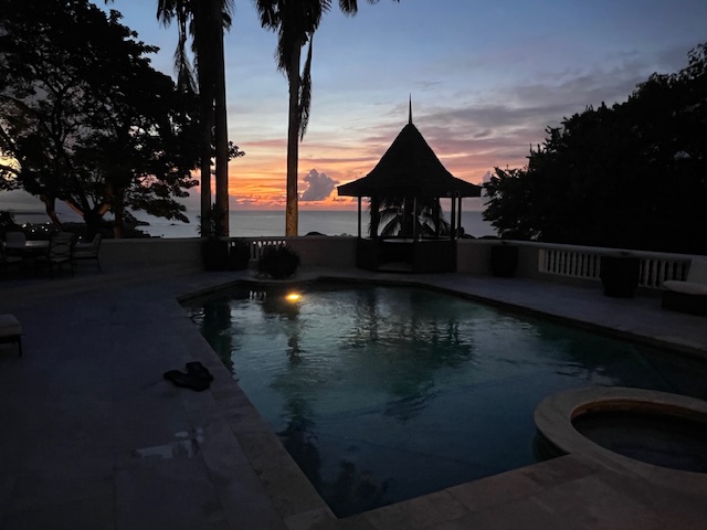 Sunset over the Caribbean, with silhouetted palms and cabana reflected in Sol Y Mar’s pool
